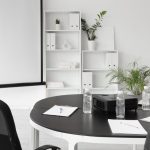 A conference room with black and white furniture, a projector screen, and a table with paper and pens.