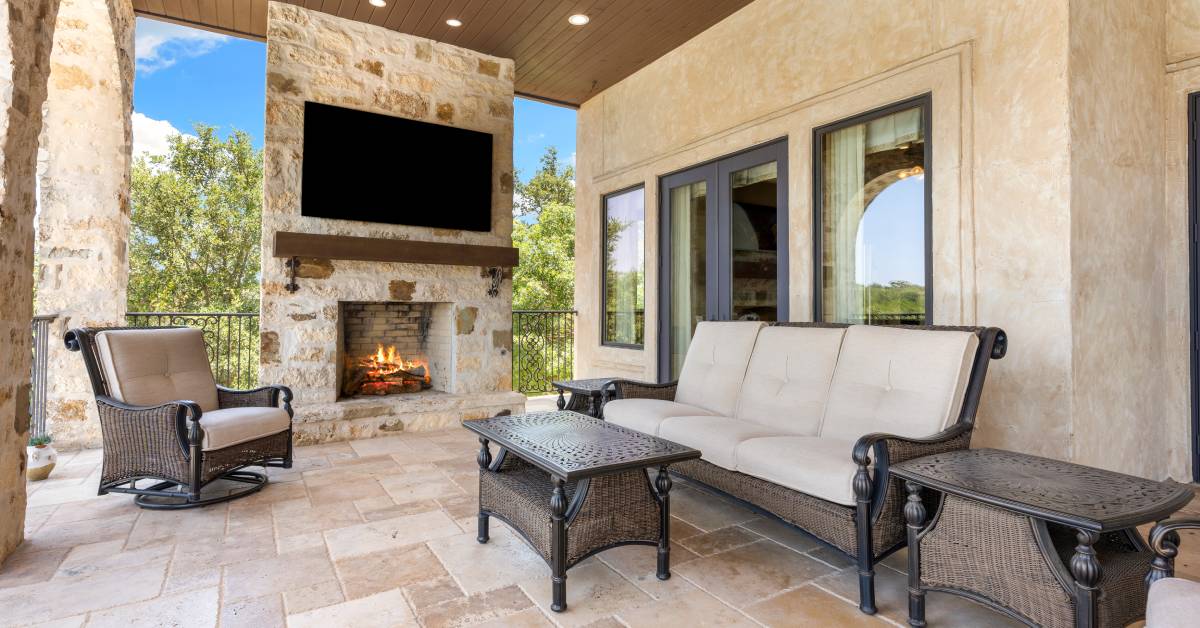 An elegant outdoor space featuring a TV mounted above a fireplace, along with modern furniture and lighting.