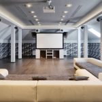 A home entertainment system featuring a projector and screen, several speakers on pillars, and minimalist couches.