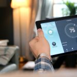 A man adjusts the temperature of his living room using a smart home application on his compact tablet.