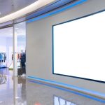 A large, blank digital display on a gray wall marks the entrance to a modern commercial clothing store.