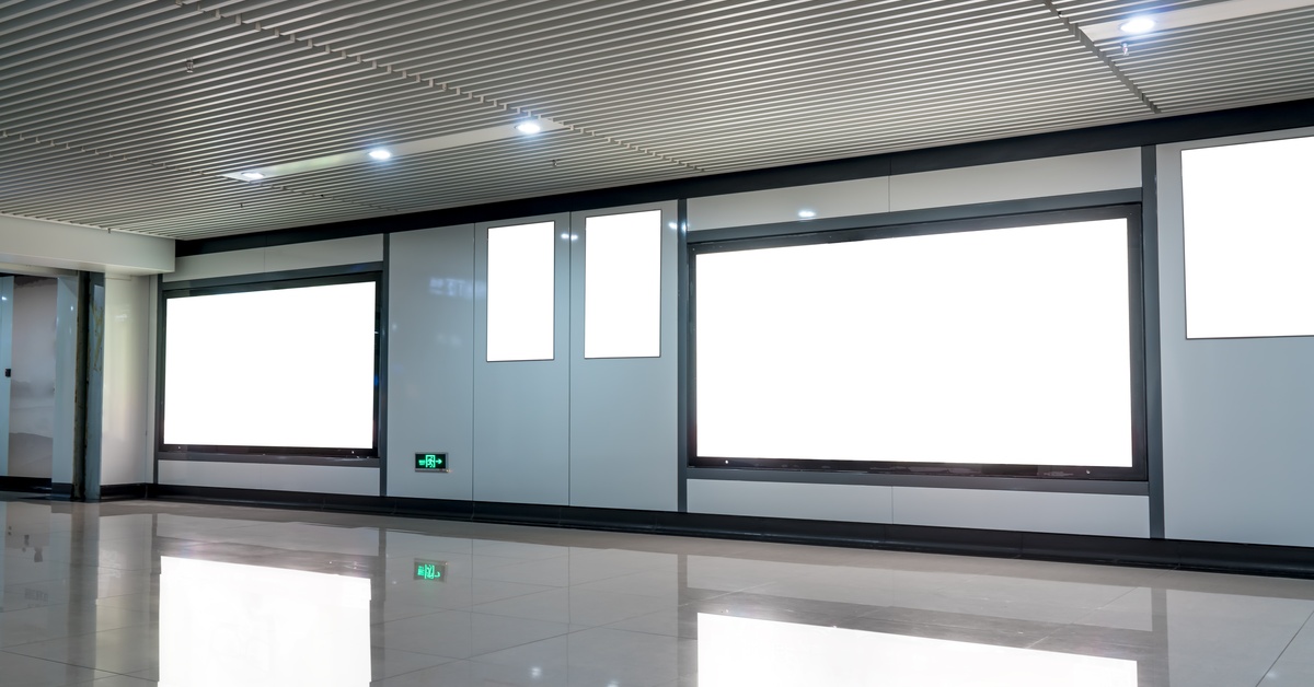 A modern, empty hallway with several blank screens on the walls. The bright displays are reflected on the floor.