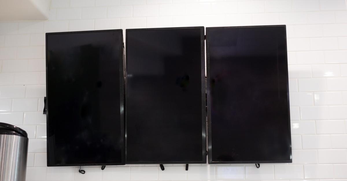 Three LCD television screens are mounted vertically on a white brick wall. They are all the same size and turned off.