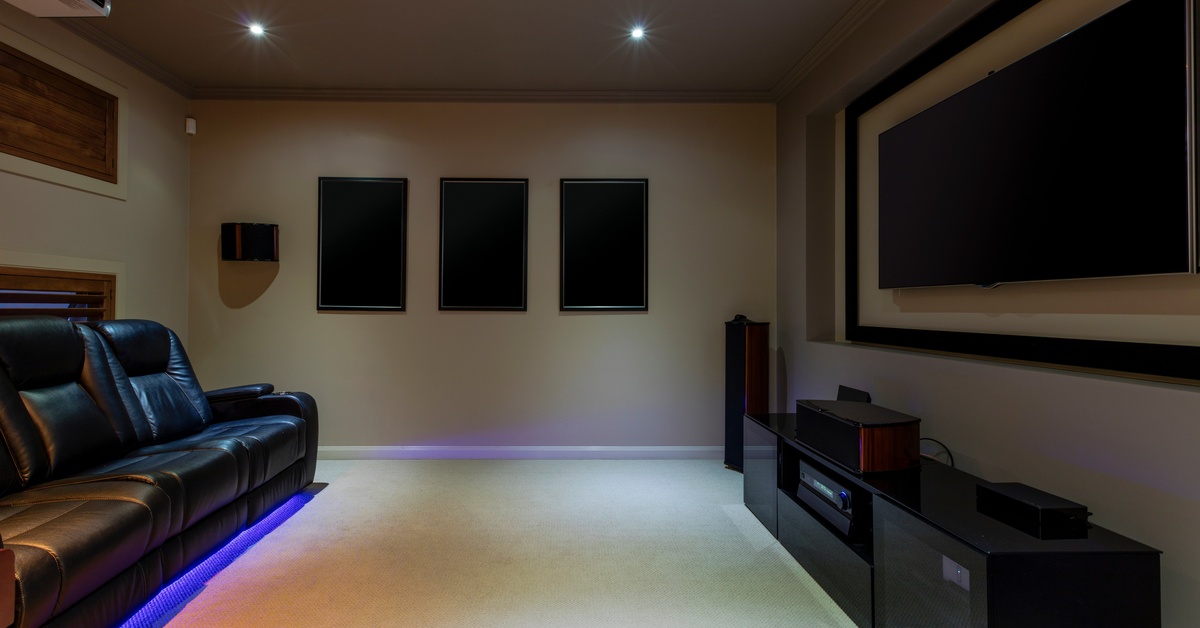 A home theater setup with a large television, a sound system, and recliners with purple lighting underneath.