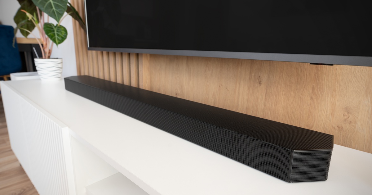 Modern setup with a flat-screen TV on a slatted wood wall, soundbar on furniture, and a potted plant to the left.