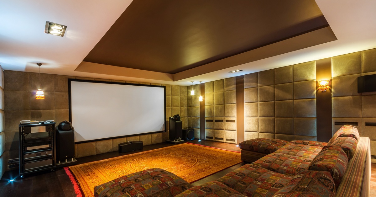 A spacious room with dim wall lighting, featuring a large projector screen and furnished with comfortable couches.
