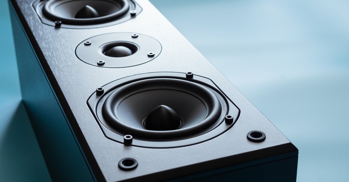 A black speaker with three drivers, including two woofers and a tweeter, set against a soft, blue background.