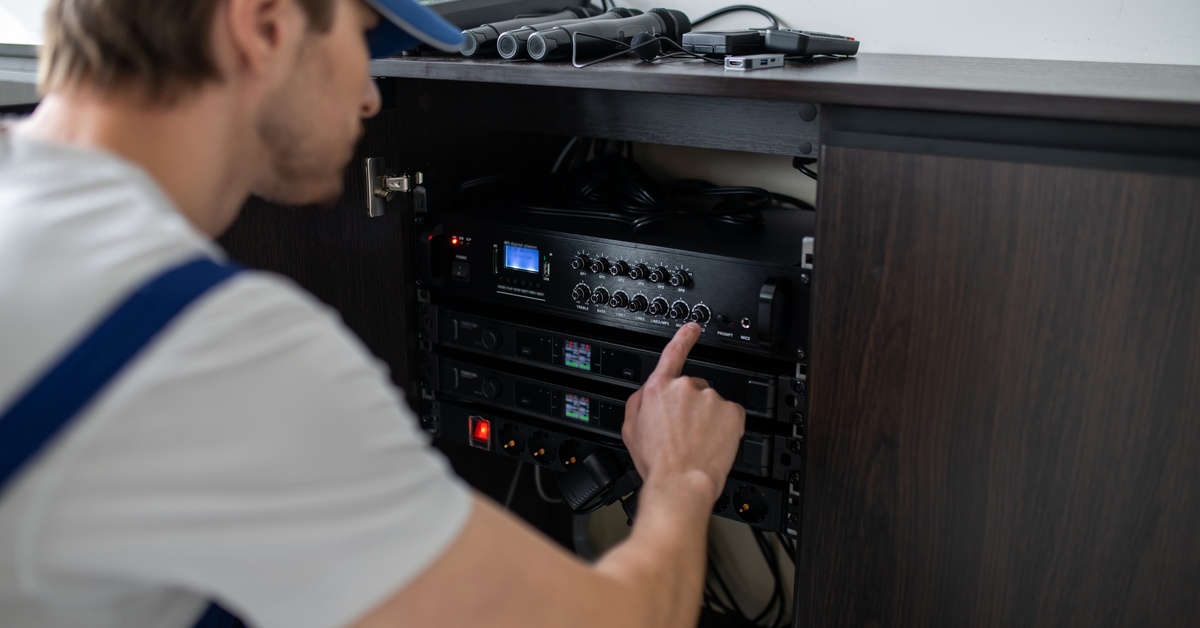 Close-up of a technician adjusting audio rack equipment inside a cabinet with visible amplifiers and connected wiring.