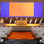 An auditorium with uplighting illuminating a digital projection screen and a table centered on the stage.