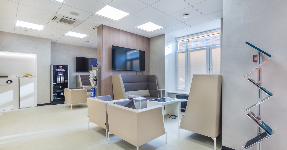 An office features bright lighting, two TVs mounted on separate walls, and seating areas positioned near the windows.