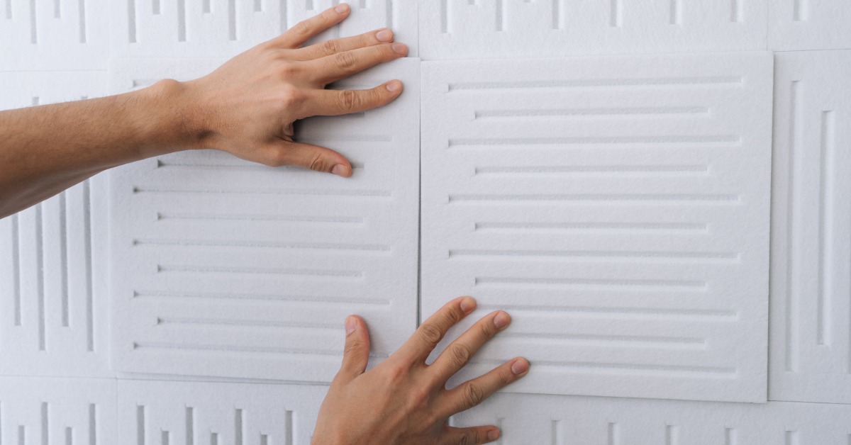 A close-up of a person placing white acoustic panels onto a wall, aligning them carefully during installation.