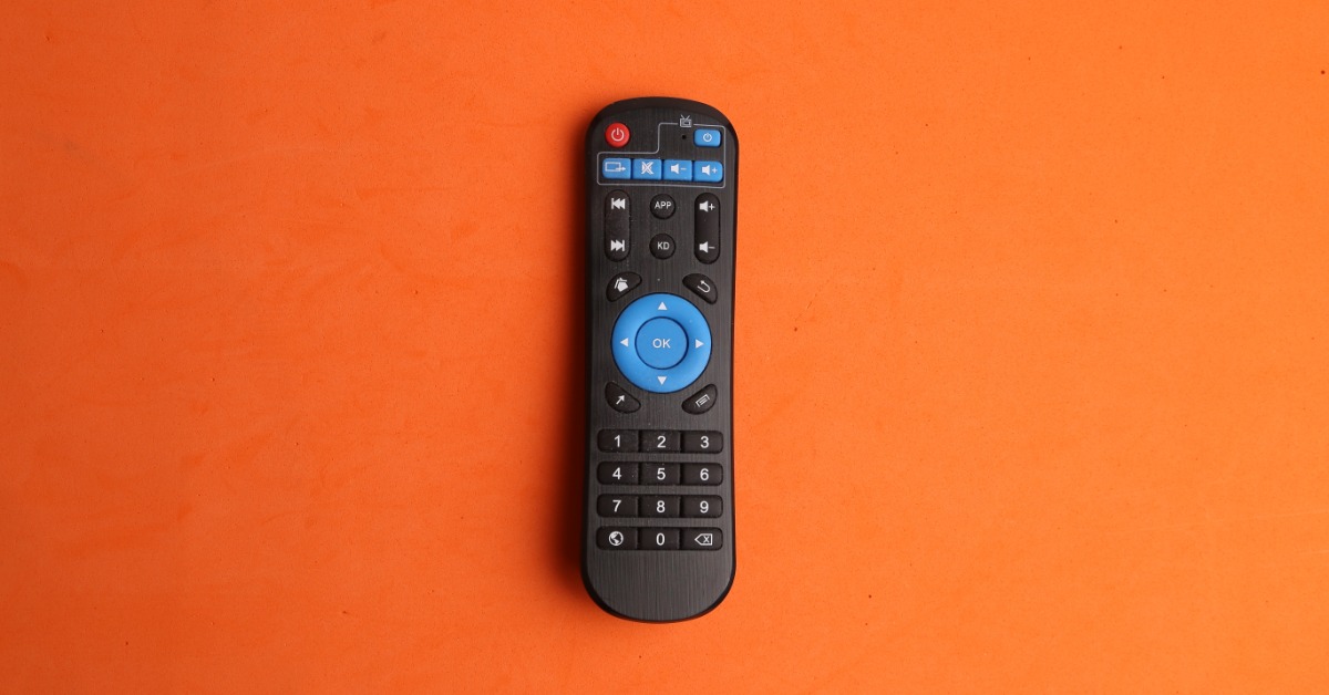 a black remote control centered on an orange surface with blue buttons and open space around the device.