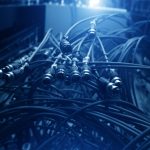 A close-up of cables plugged into a server panel with metal connectors and blurred equipment in the background.